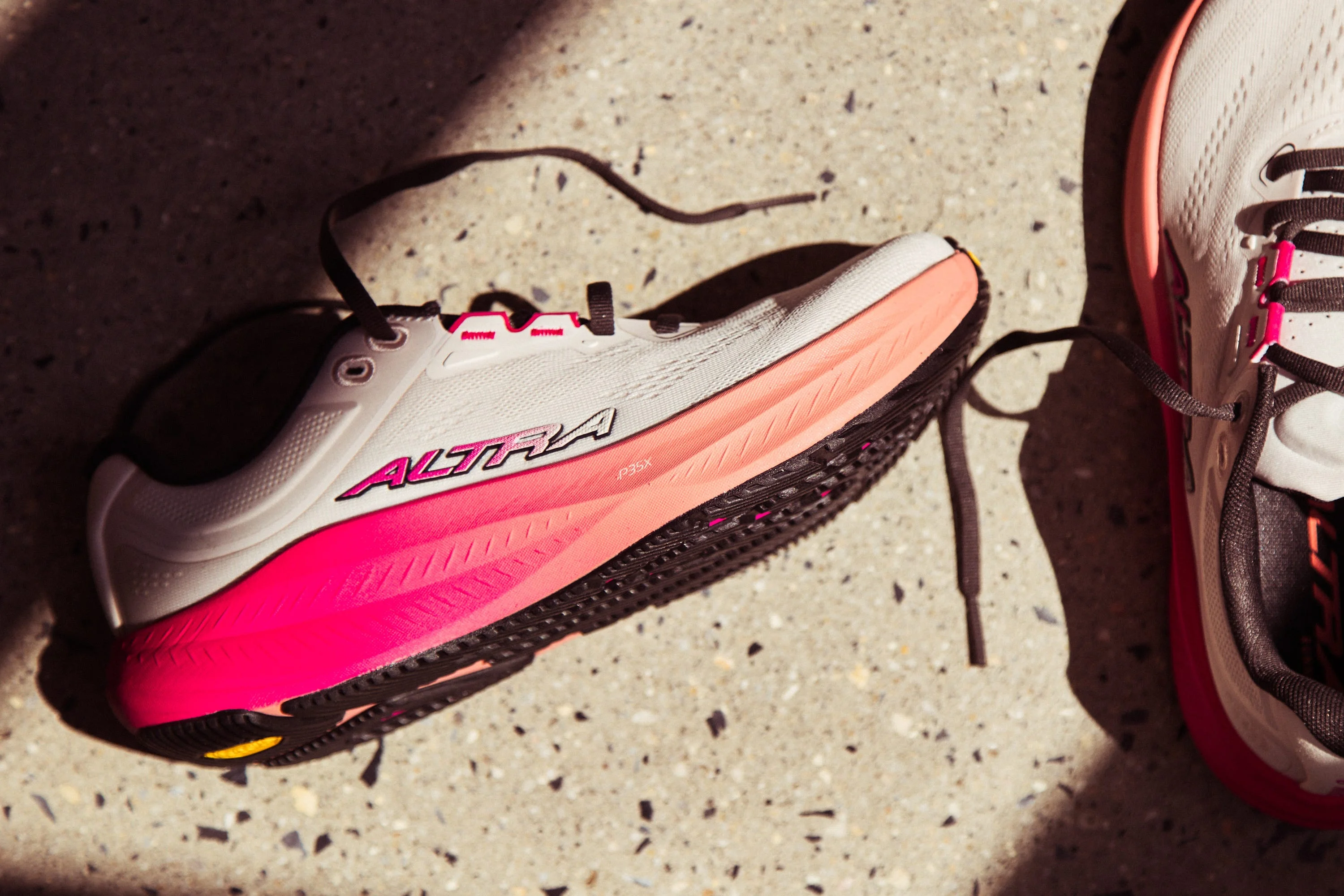 A pair of Altra running shoes featuring a white and pink design on a textured surface. A pair of Altra running shoes featuring a white and pink design on a textured surface.
