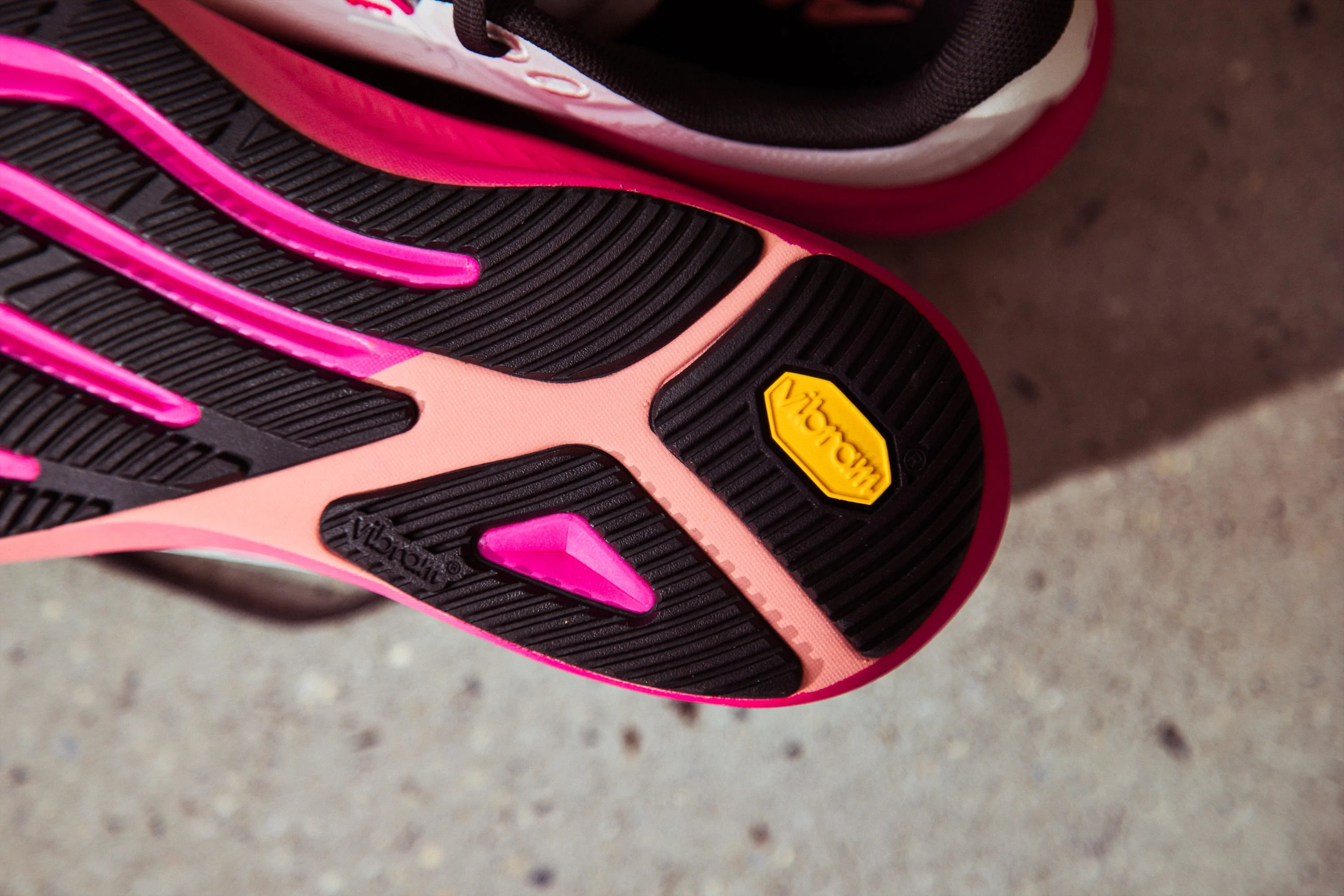 Shoe sole featuring pink and black rubber with a yellow Vibram logo for enhanced traction and durability. Shoe sole featuring pink and black rubber with a yellow Vibram logo for enhanced traction and durability.