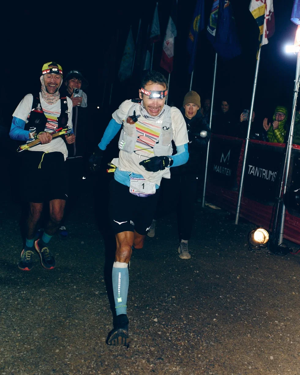 Runners crossing the finish line of a night race, celebrating their accomplishment amidst cheering spectators.