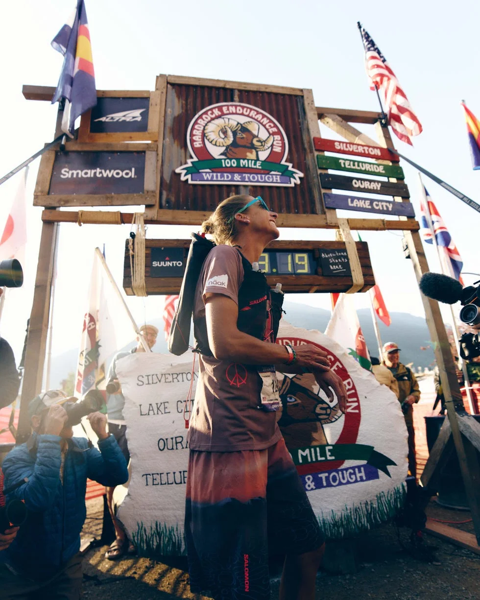 Runner celebrating at the Hardrock Endurance Run finish line, surrounded by flags and photographers. Runner celebrating at the Hardrock Endurance Run finish line, surrounded by flags and photographers.